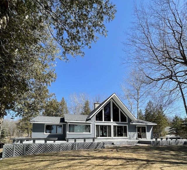 view of front facade featuring a chimney, a wooden deck, and a front lawn