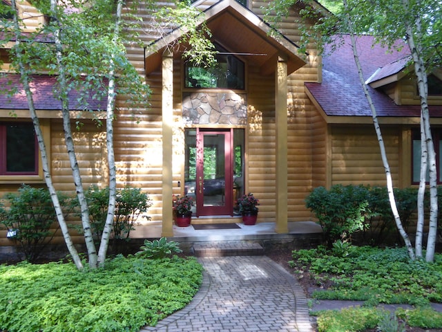 view of exterior entry with stone siding, faux log siding, and a shingled roof