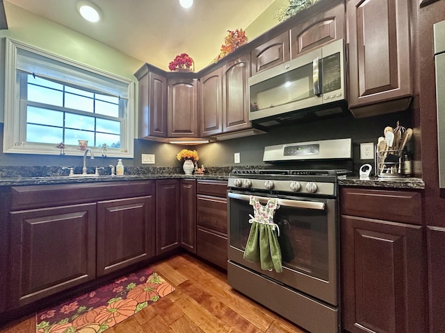 kitchen with a sink, dark stone countertops, light wood finished floors, and stainless steel appliances