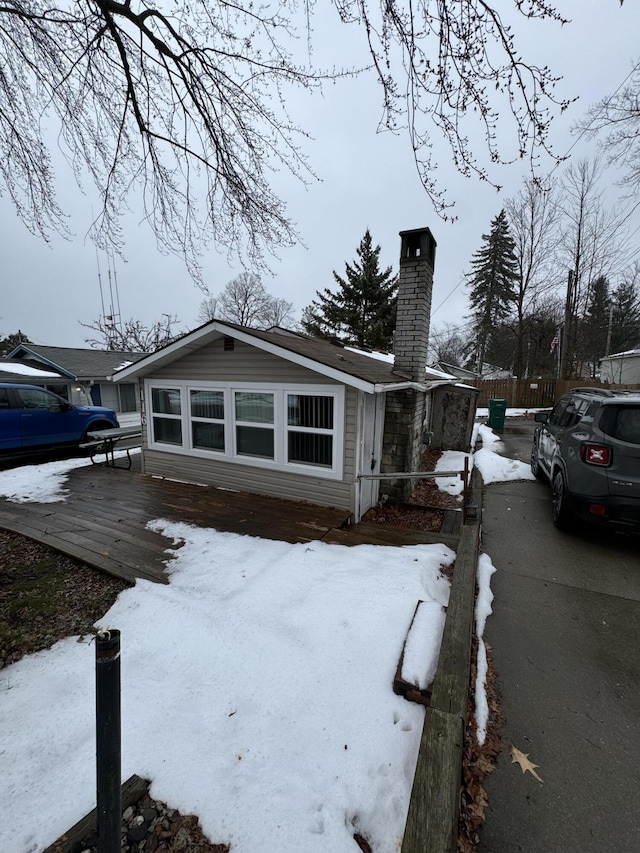 snow covered property featuring a wooden deck, a chimney, and fence