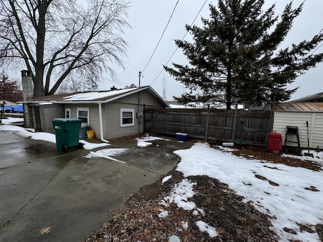 view of snow covered exterior featuring a chimney and fence