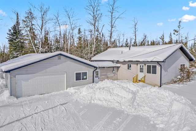 snow covered rear of property featuring entry steps and a garage