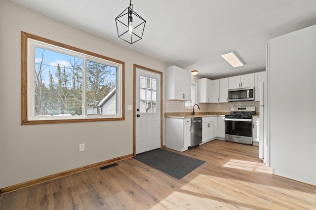 kitchen featuring a sink, decorative backsplash, stainless steel appliances, white cabinets, and light wood-style floors