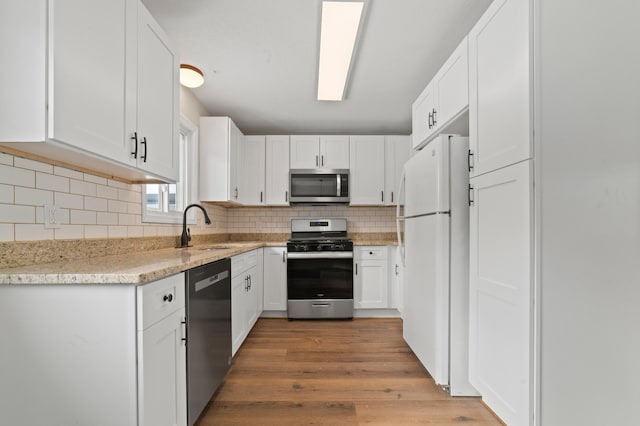 kitchen featuring light wood-type flooring, a sink, stainless steel appliances, white cabinets, and decorative backsplash