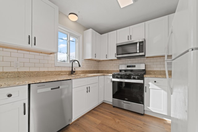 kitchen featuring decorative backsplash, light wood-style flooring, white cabinets, stainless steel appliances, and a sink