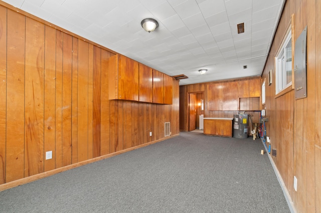 interior space with visible vents, baseboards, electric water heater, and wooden walls