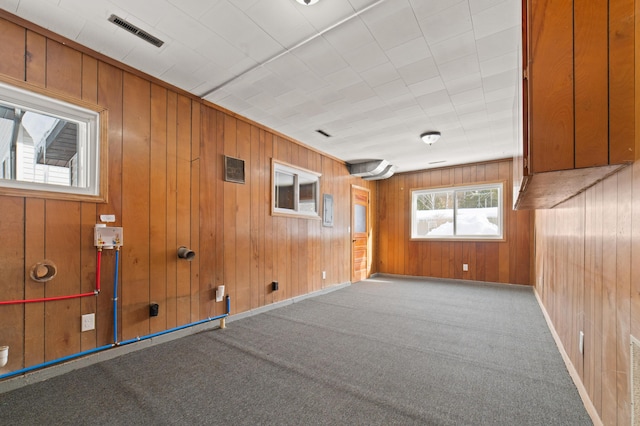 carpeted spare room featuring visible vents, baseboards, and wood walls