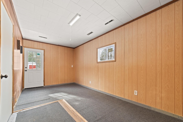 spare room featuring visible vents, wood walls, crown molding, and carpet