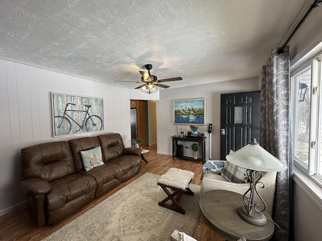 living area featuring baseboards, a textured ceiling, a ceiling fan, and wood finished floors