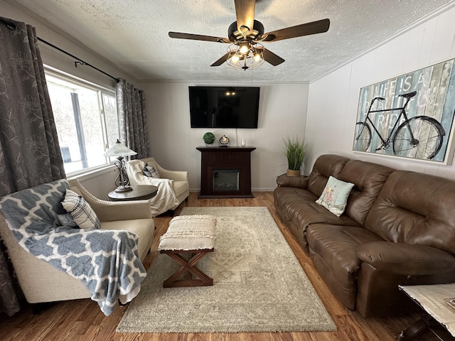 living room with a fireplace, a textured ceiling, wood finished floors, and a ceiling fan