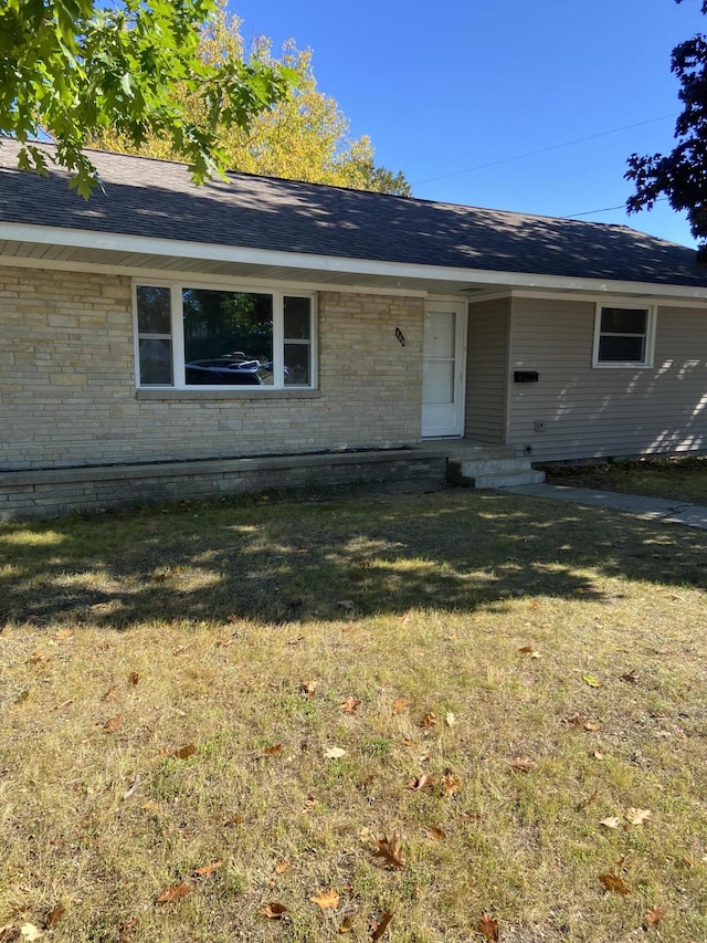 view of front of house featuring brick siding, a shingled roof, and a front yard