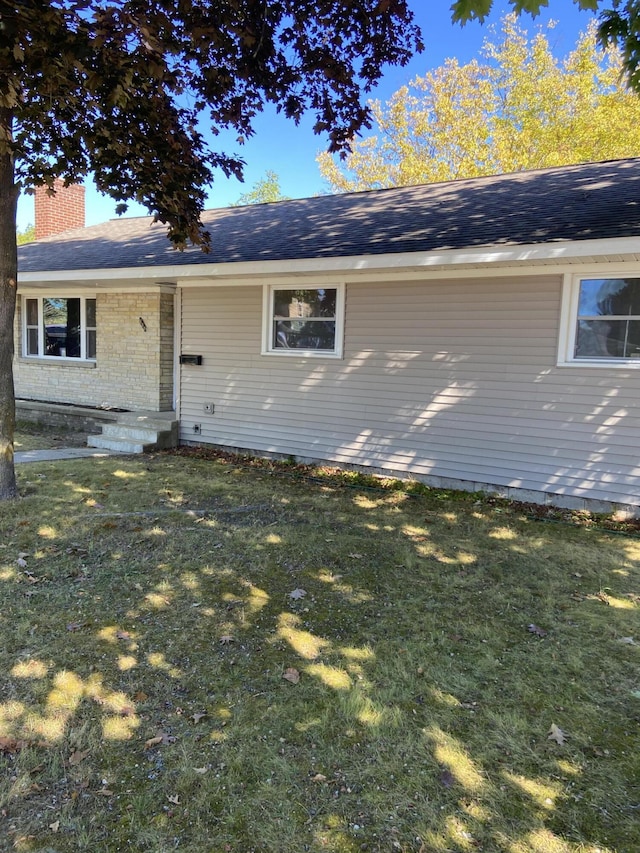 view of front of home with brick siding, a chimney, a front yard, and roof with shingles