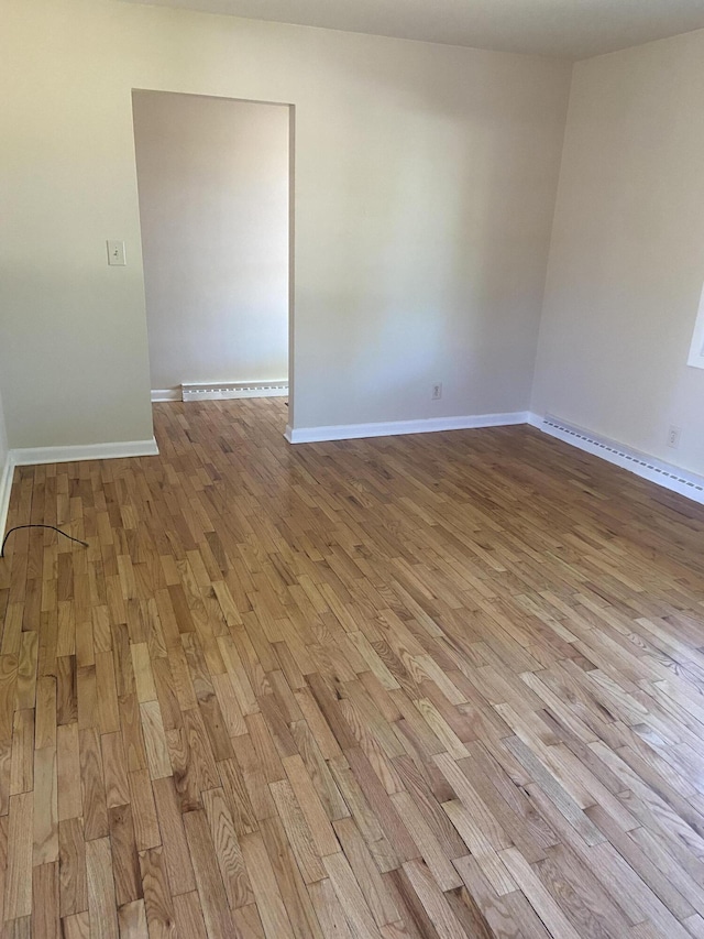 spare room featuring baseboards, light wood finished floors, and a baseboard radiator