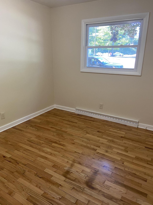 spare room with a baseboard heating unit, baseboards, and wood finished floors