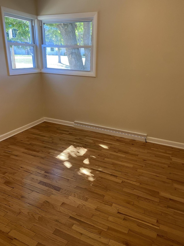 empty room featuring wood finished floors, baseboards, and a baseboard radiator