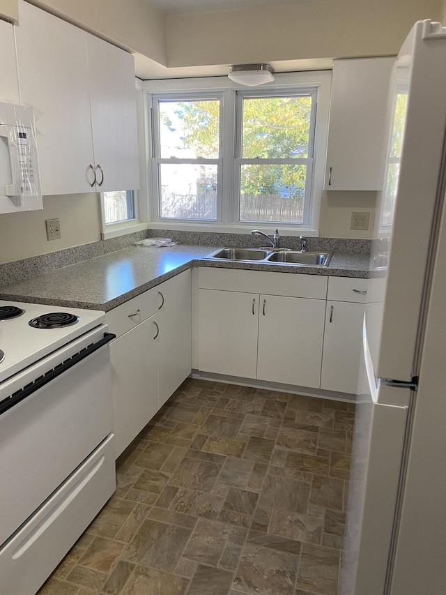 kitchen featuring a sink, white appliances, stone finish floor, and white cabinetry