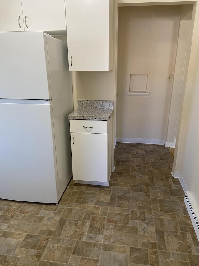 kitchen featuring light stone counters, freestanding refrigerator, white cabinets, baseboards, and baseboard heating