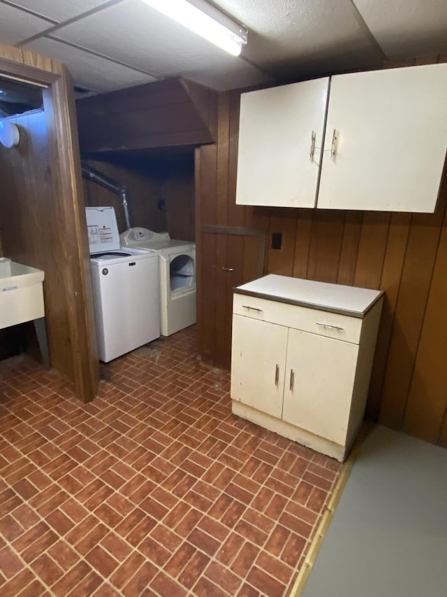 clothes washing area with brick patterned floor, cabinet space, independent washer and dryer, and wood walls