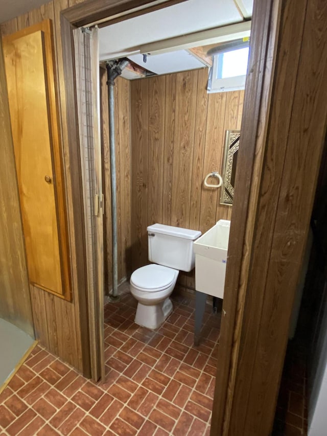 half bath featuring wood walls, brick patterned floor, and toilet