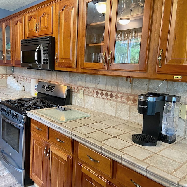 kitchen featuring brown cabinetry, glass insert cabinets, stainless steel range with gas cooktop, and black microwave