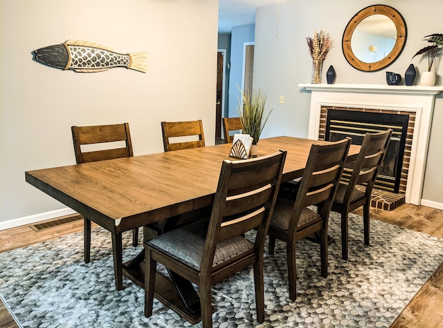 dining room featuring a fireplace, wood finished floors, visible vents, and baseboards