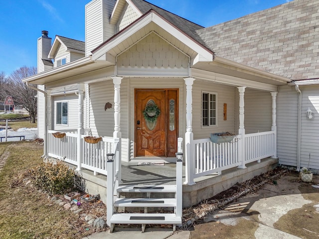 entrance to property featuring covered porch and roof with shingles