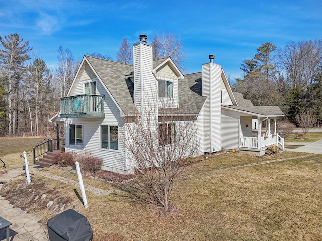 view of side of property featuring a balcony, roof with shingles, covered porch, a chimney, and a lawn