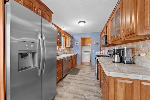 kitchen featuring brown cabinets, a sink, washer / clothes dryer, stainless steel appliances, and tile counters