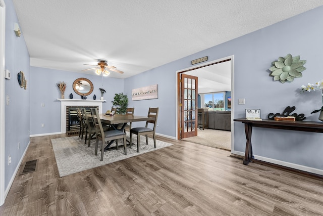 dining space with wood finished floors, baseboards, visible vents, ceiling fan, and a textured ceiling