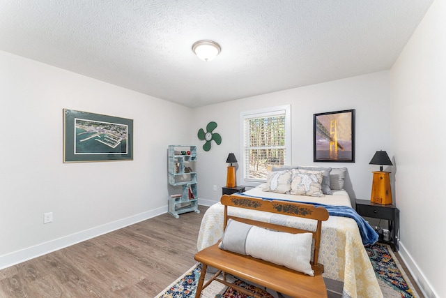 bedroom featuring a textured ceiling, baseboards, and wood finished floors