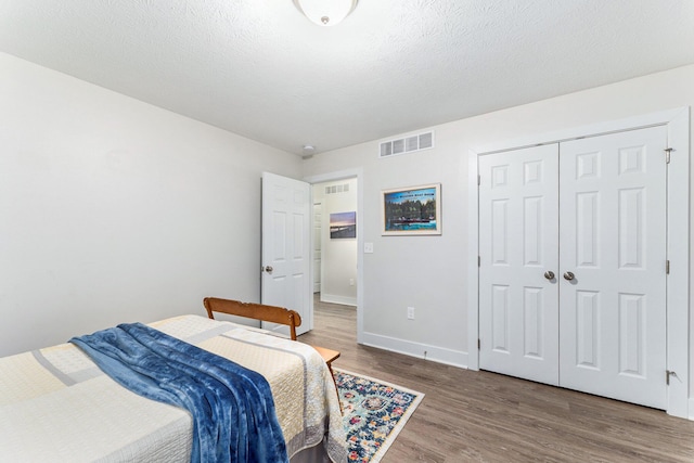 bedroom with visible vents, a textured ceiling, baseboards, and wood finished floors