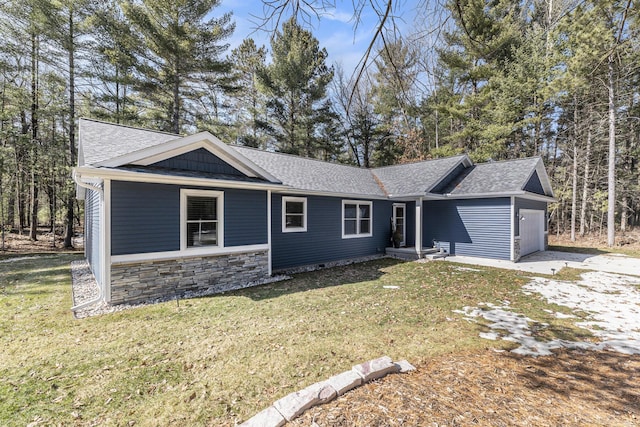 single story home with stone siding, an attached garage, a front lawn, and roof with shingles