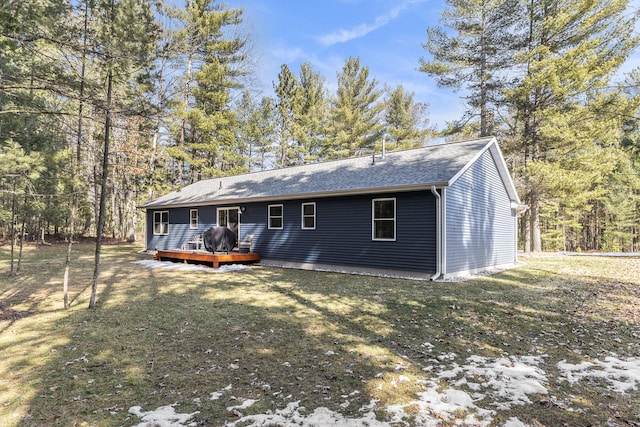 rear view of house featuring a lawn, a deck, and roof with shingles