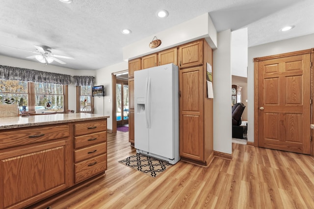 kitchen featuring a textured ceiling, white fridge with ice dispenser, brown cabinetry, and light wood finished floors