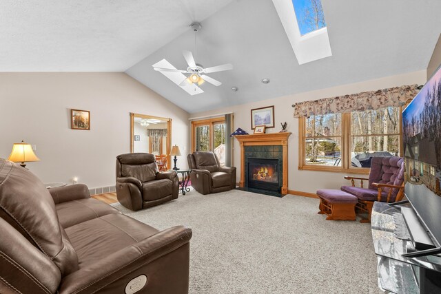 living room with lofted ceiling with skylight, carpet, baseboards, ceiling fan, and a tile fireplace