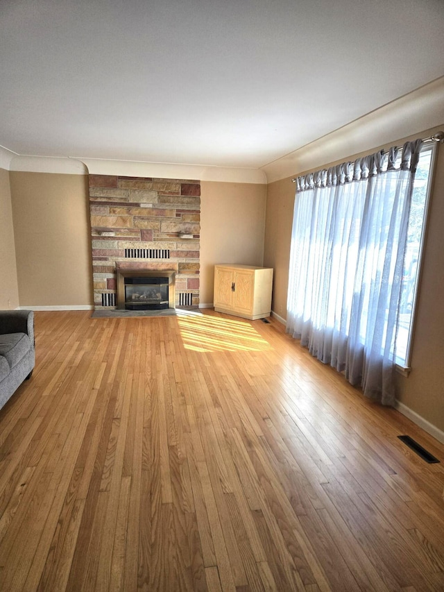 unfurnished living room with visible vents, baseboards, hardwood / wood-style floors, ornamental molding, and a stone fireplace