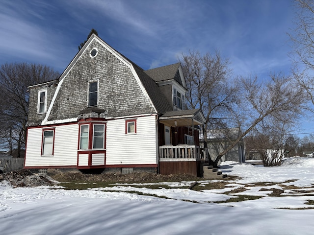 view of snowy exterior featuring a gambrel roof, roof with shingles, and covered porch