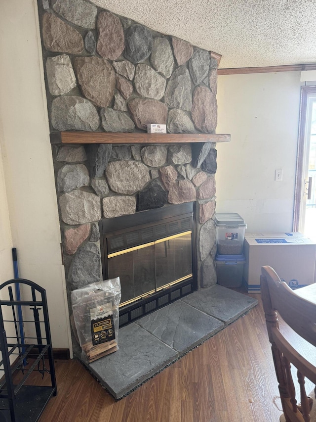 room details featuring a stone fireplace, ornamental molding, a textured ceiling, and wood finished floors