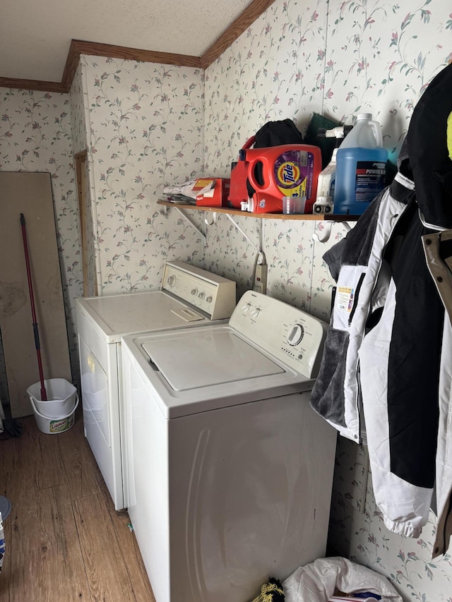 laundry area with wallpapered walls, ornamental molding, laundry area, wood finished floors, and washer and dryer