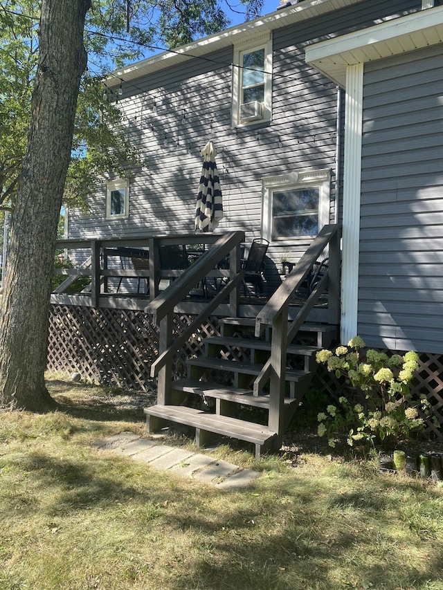 back of property featuring a wooden deck, a lawn, and stairs