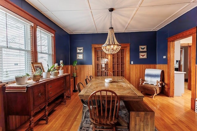 dining room featuring wooden walls, a notable chandelier, hardwood / wood-style floors, and wainscoting