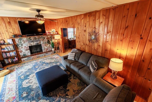 living room featuring a stone fireplace, wood walls, and a ceiling fan