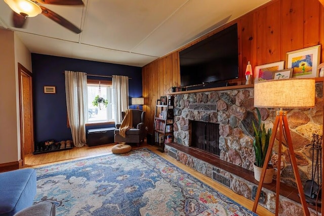 living area featuring a ceiling fan, wood finished floors, a fireplace, and wood walls