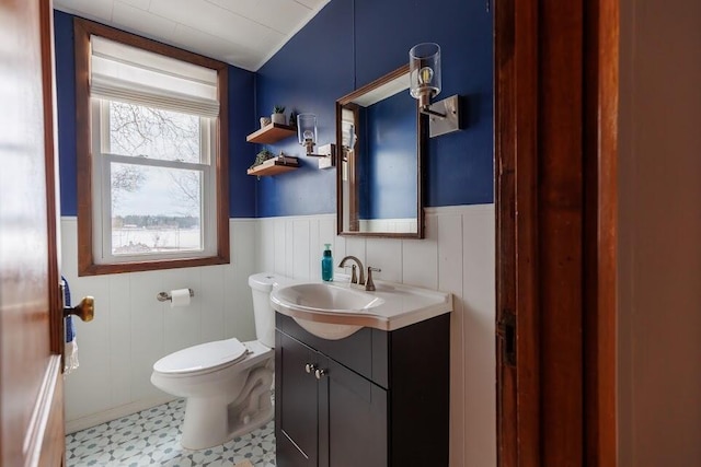 half bath with tile patterned floors, wainscoting, toilet, and vanity