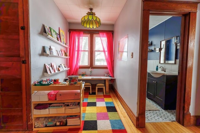 hall with light wood-style flooring, baseboards, and a sink