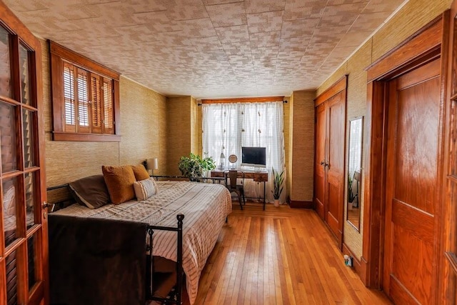 bedroom with wallpapered walls, multiple windows, multiple closets, and light wood finished floors