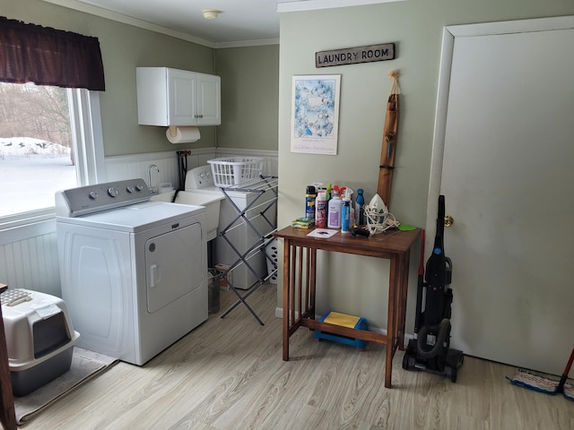 laundry area featuring light wood finished floors, cabinet space, wainscoting, crown molding, and washer and clothes dryer