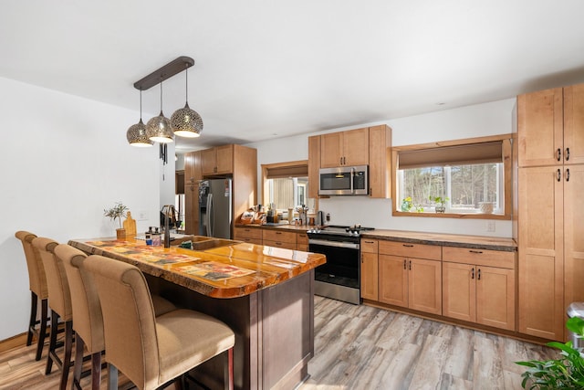 kitchen featuring a breakfast bar, light wood finished floors, stainless steel appliances, and a sink