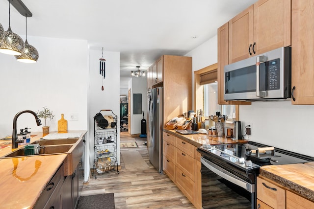 kitchen featuring light brown cabinets, light wood-style flooring, hanging light fixtures, stainless steel appliances, and a sink