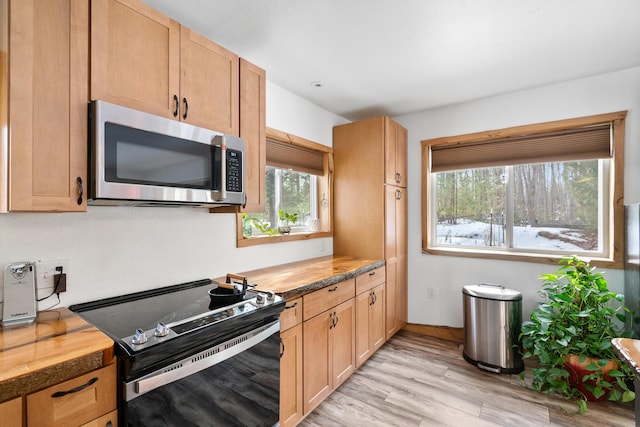 kitchen featuring stainless steel microwave, wooden counters, light wood-style floors, and electric range oven